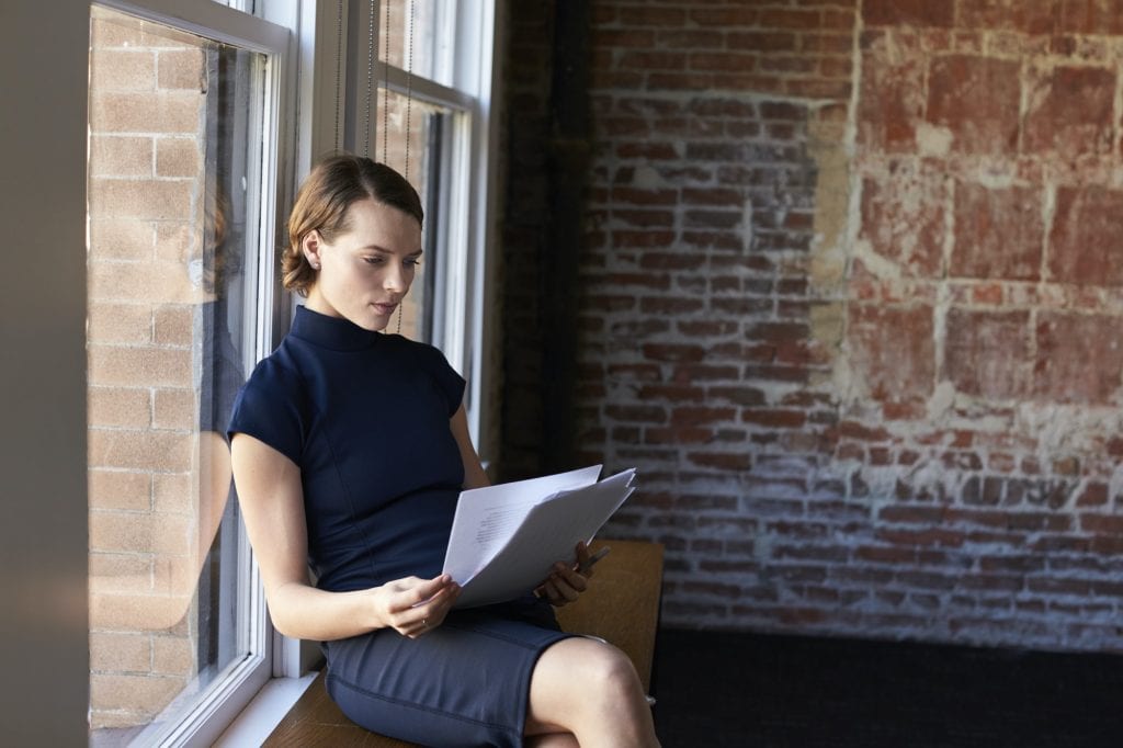 Businesswoman Sitting By Window Reading Documents